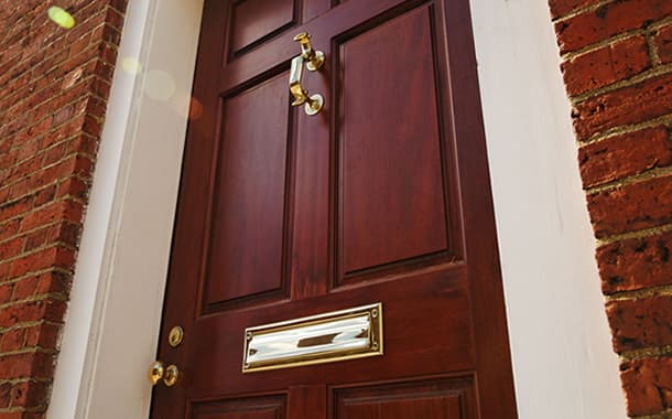 Wood-panel front door with a brass knocker in a brick entry