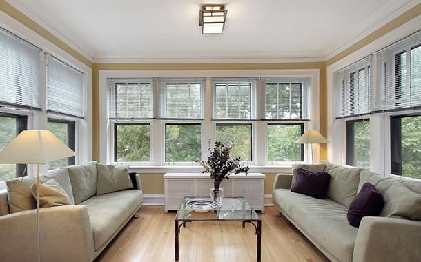Sunroom lined with white double-hung windows looking out to green trees